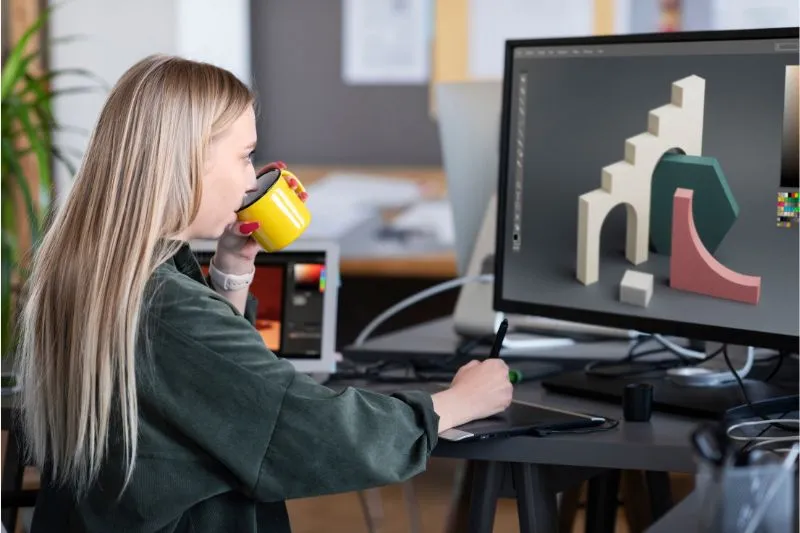 A 3D animation designer at a studio, sipping coffee while working on a digital 3D model on a computer screen, illustrating the creative process in a professional 3D animation studio.