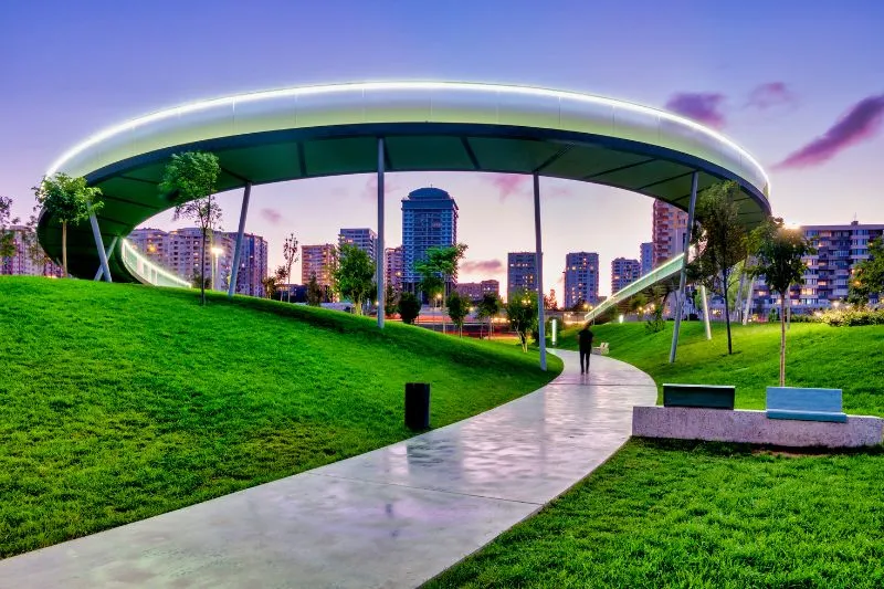 A 3D architectural animation rendering of an urban park with a modern, illuminated canopy structure, walking paths, and green spaces, showcasing the design and potential uses of the park for public and city officials through detailed visualizations.