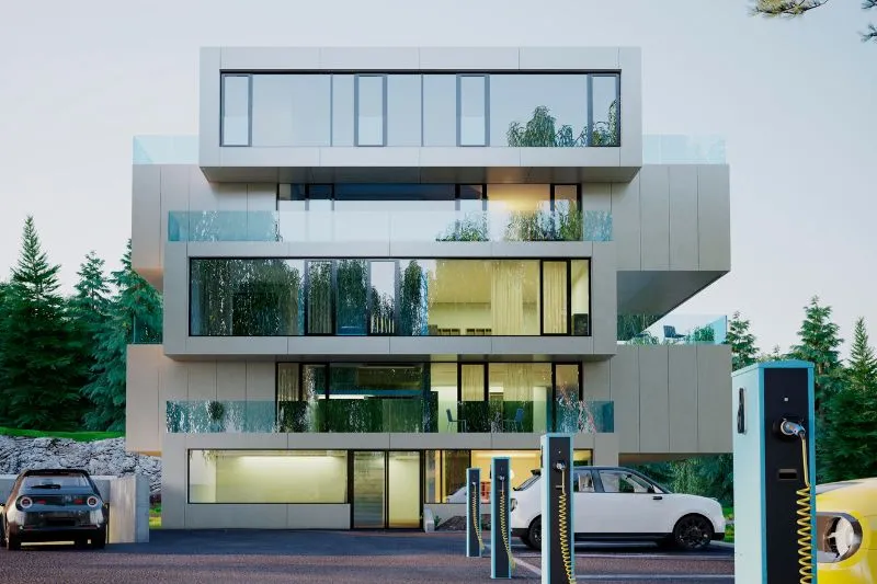 A 3D architectural animation rendering of a modern residential complex with large glass windows and electric vehicle charging stations, surrounded by greenery, showcasing the exterior design and amenities to attract buyers and investors.