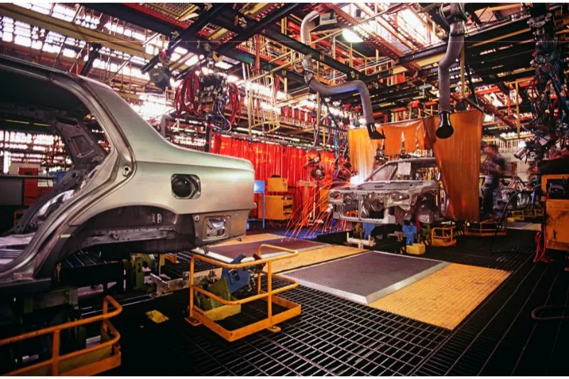 An automotive manufacturing plant with car frames on the assembly line, illustrating the use of 3D product animation to showcase new electric vehicle designs, features, and technologies to attract investors and customers in the automotive industry.