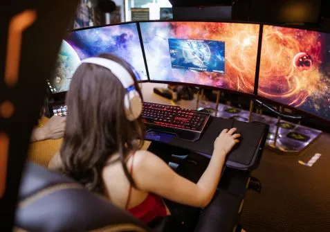 A game designer wearing headphones, working at a multi-monitor setup displaying a space-themed game, highlighting collaboration between 3D modelers and developers to create innovative and engaging games.