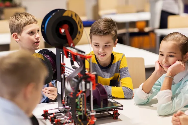 A group of children in a classroom interacting with a 3D printer, representing the use of 3D animation and technology in education to make learning engaging, visually appealing, and easier to understand.